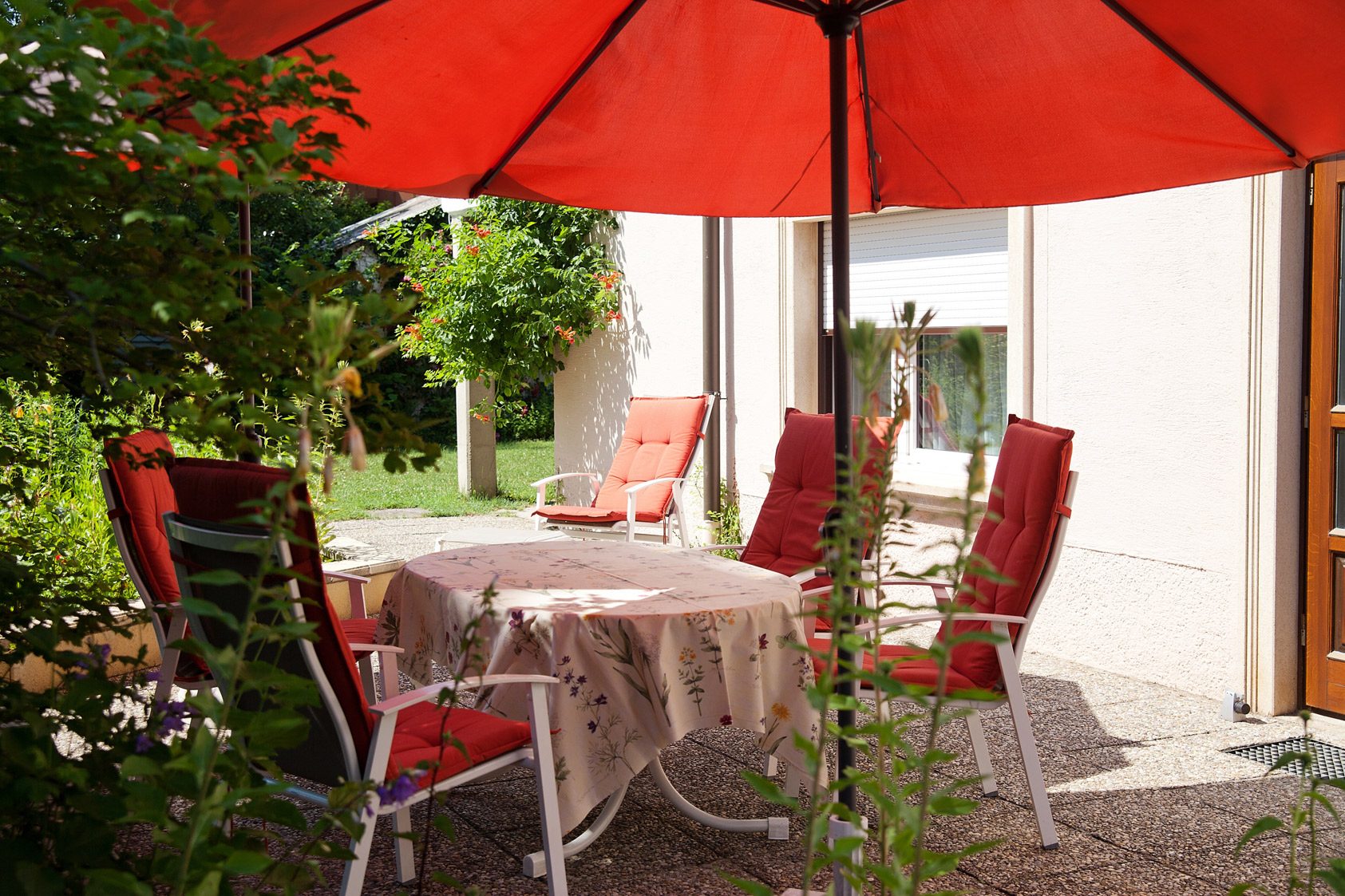 Terrasse mit Tisch, Stühlen und rotem Sonnenschirm